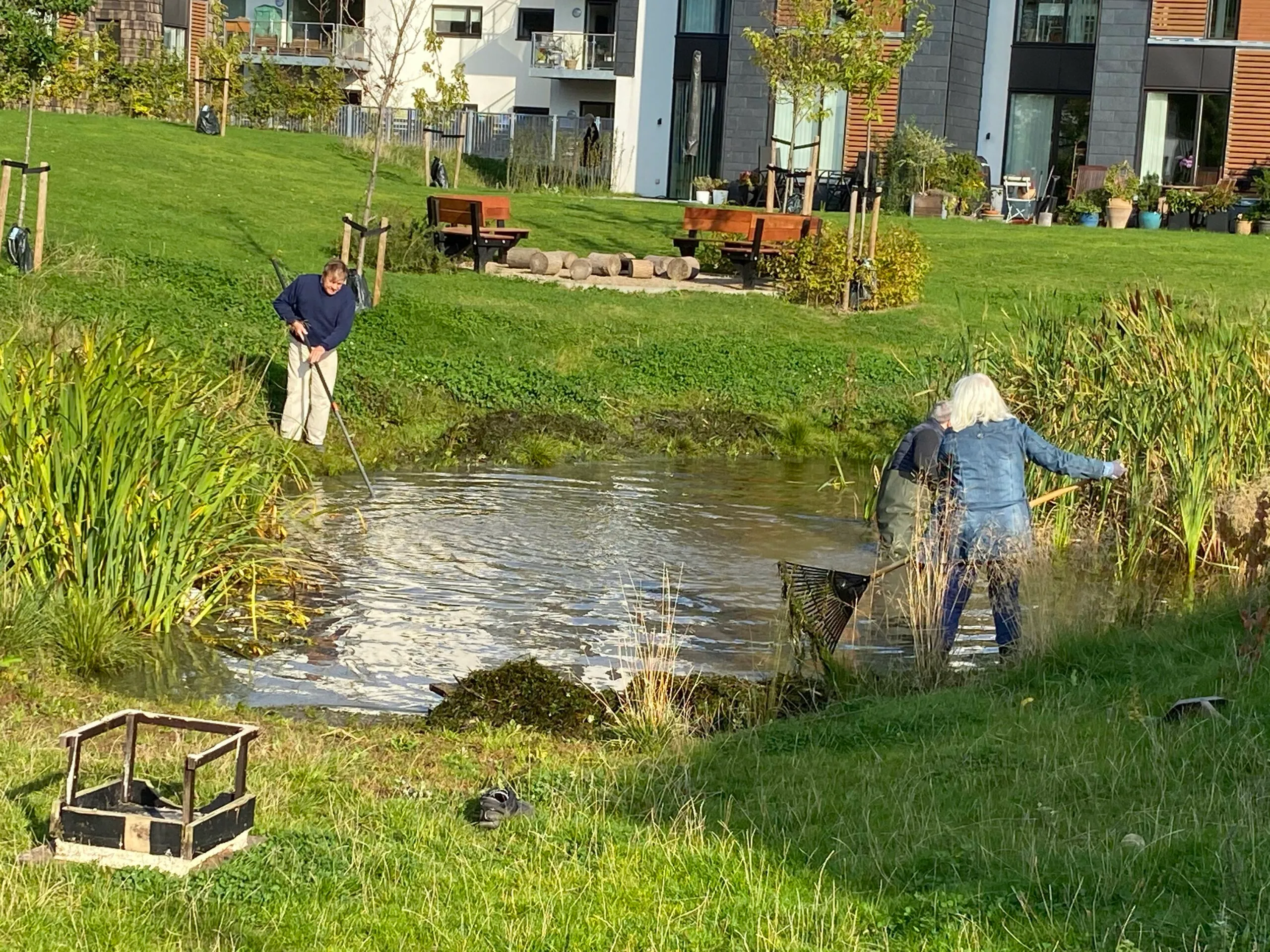 Beboere arbejder med river og redskaber ved regnvandsbassinet foran lejlighederne